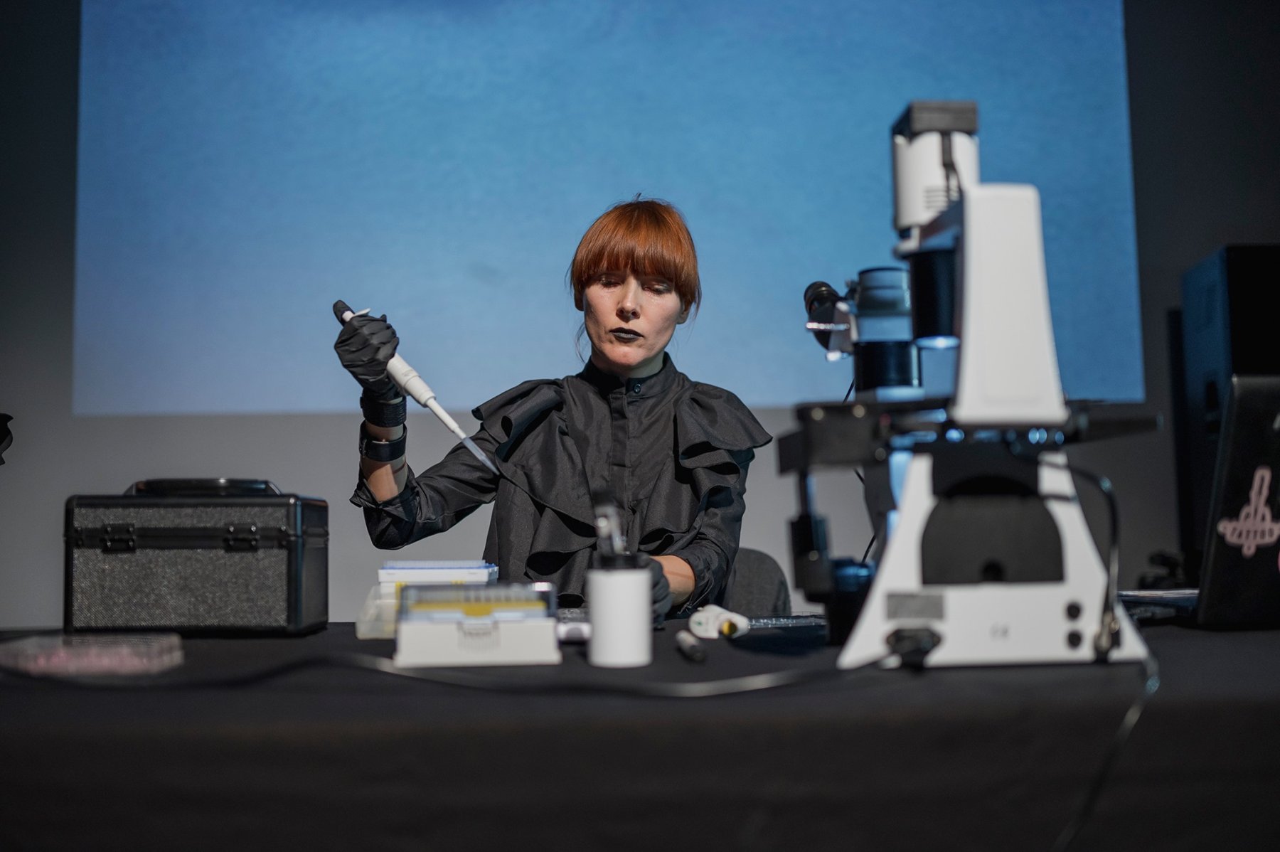 A woman sitting at a desk with a laboratory tool and micrscope